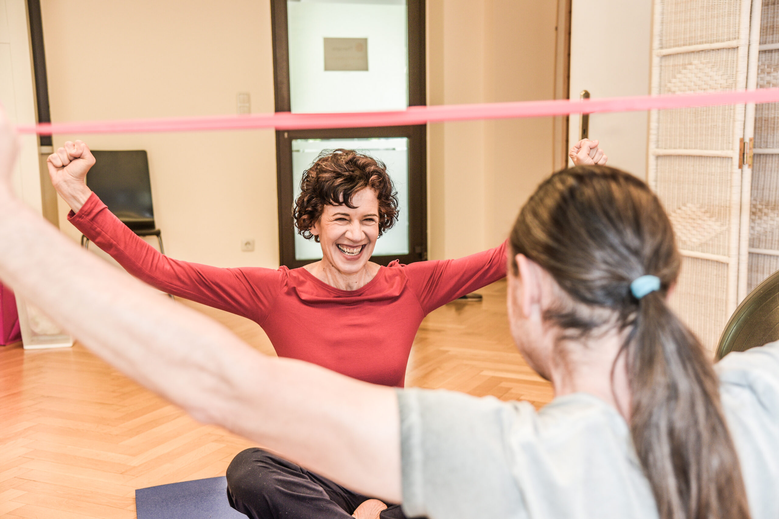 Patient macht Übung mit Theraband und sieht dabei die Physiotherapeutin an